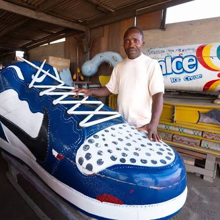 Ghanaian man standing next to a fancy coffin shoe shapped