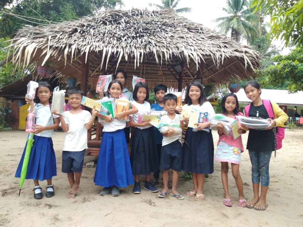 Young children holding gifts in front of hut in Philippines