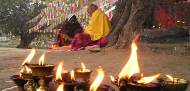 Buddhist monk beneath colourful prayer flags with butter lamps in the foreground