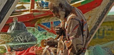 Ghanaian fisherman repairing fishing nets beside colourful fishing boats